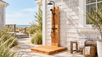 Cedar outdoor shower with black rainfall showerhead, handheld sprayer, and wooden platform beside a shingle-sided home.