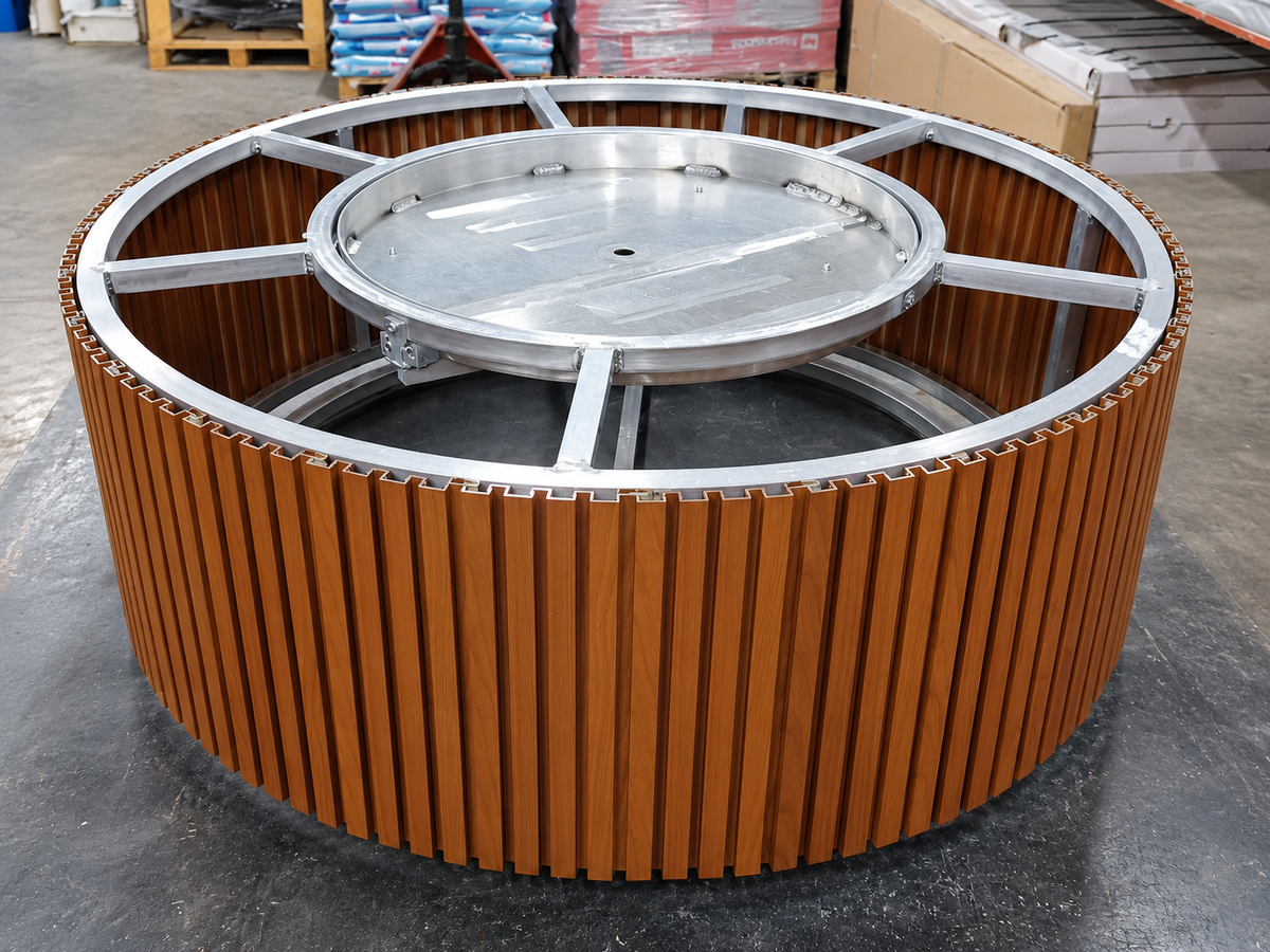 EZ Finish Firefly 48-inch round aluminum-clad fire pit enclosure with optional round burner pan installed, shown during assembly in a workshop.