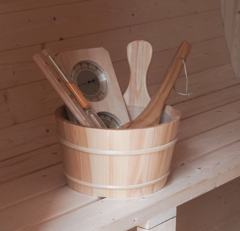 Wooden sauna bucket holding a ladle, thermometer, and other accessories on a bench inside the Aleko Liatris sauna.