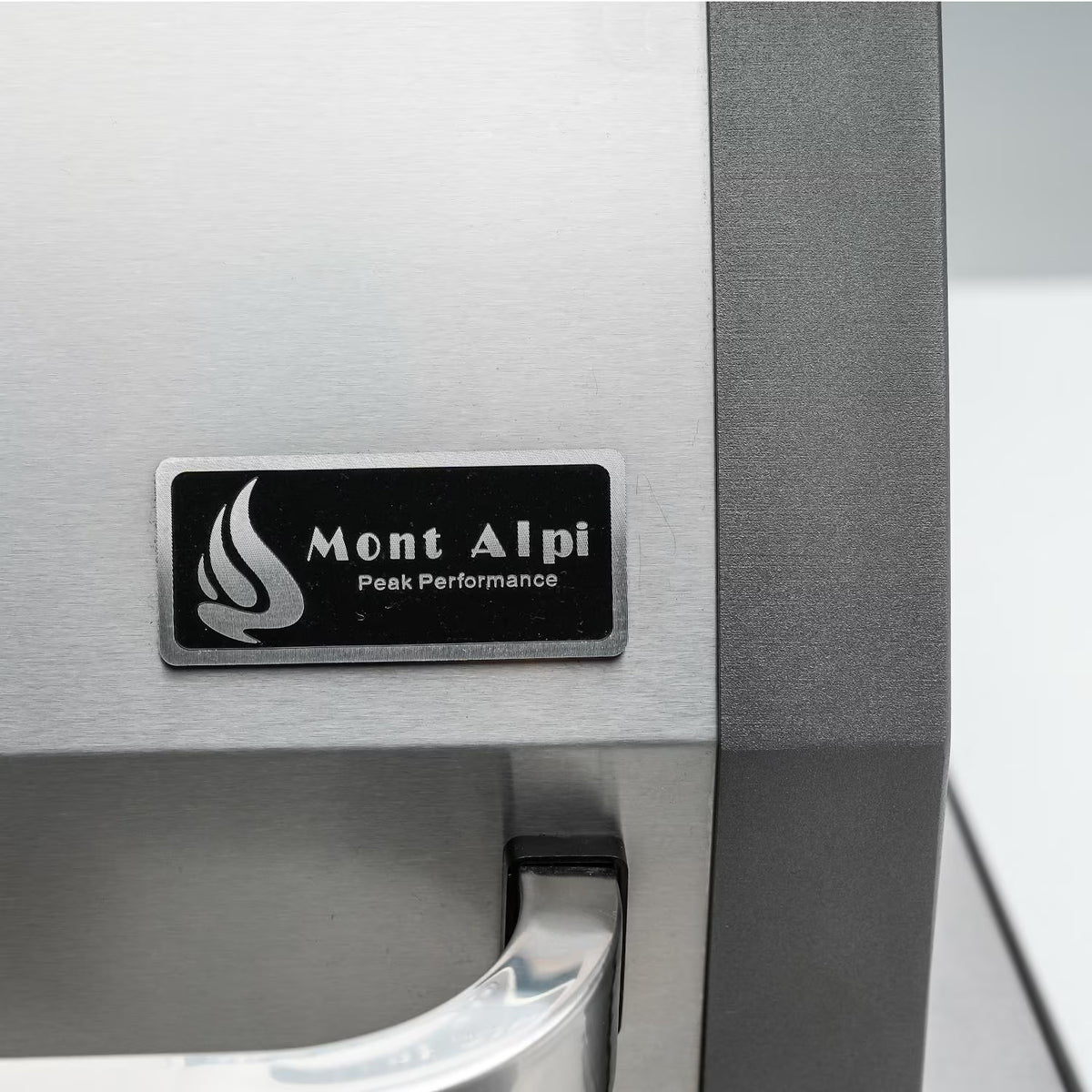 Close-up of Mont Alpi manufacturer badge and stainless steel grill hood handle on the 805 Deluxe outdoor kitchen