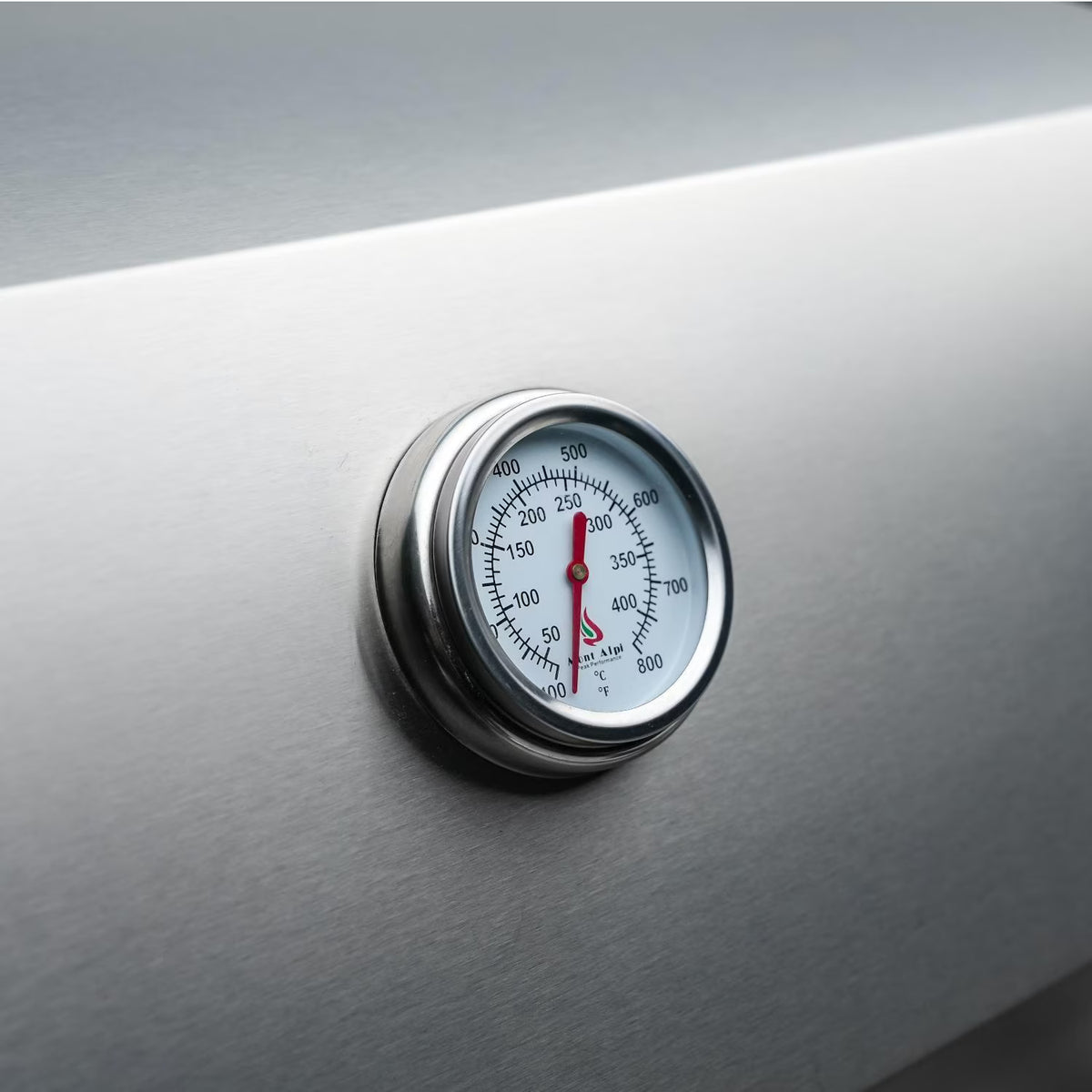 Close-up of built-in analog temperature gauge on the stainless steel grill hood of the Mont Alpi 805 Deluxe outdoor kitchen