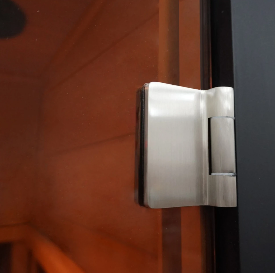 Close-up of the ALEKO Oasis 1-Person Infrared Sauna tempered glass door hinge with black frame and warm hemlock interior