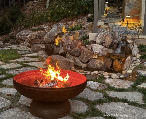 Ohio Flame Patriot fire pit burning in a landscaped backyard with stone patio and waterfall